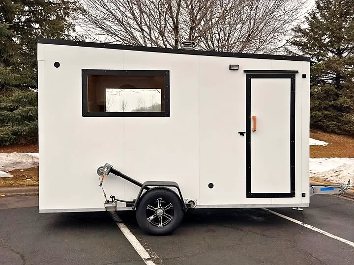 The sauna trailer: white aluminum body, black-framed window and door