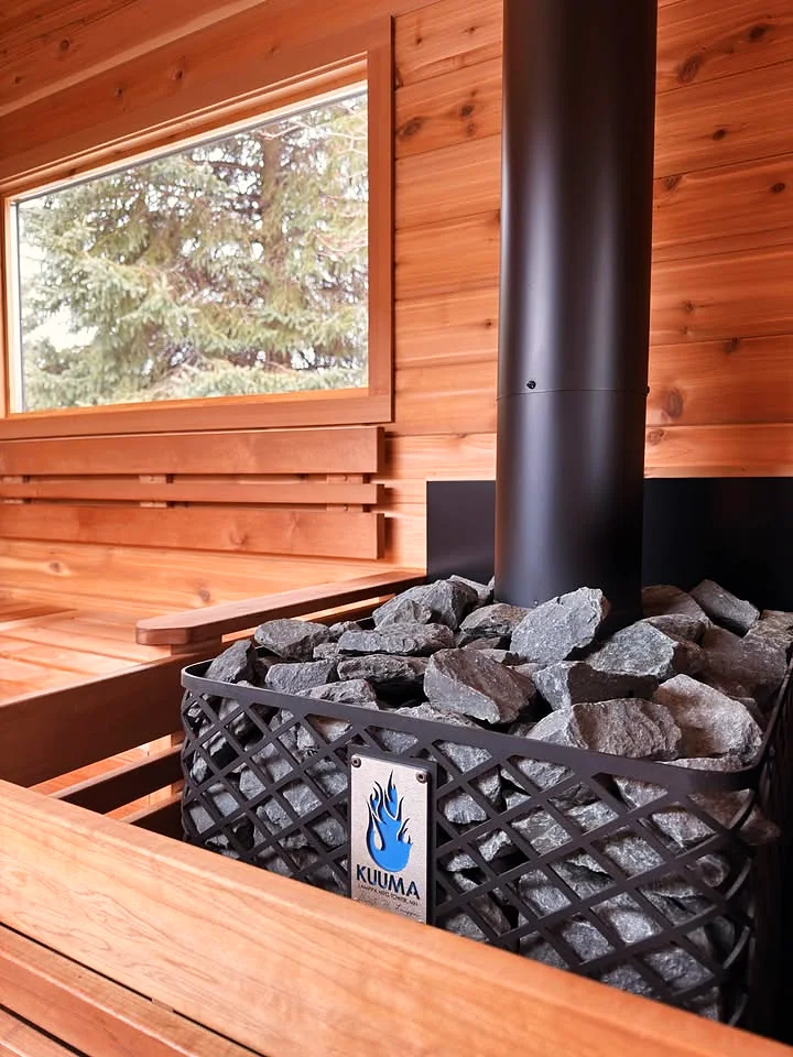 The Kuuma Blue Flame stove with its basket of sauna stones and black chimney pipe
